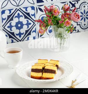 Malaysisches Gericht Kek Lapis Sarawak oder Sarawak Layered Cake auf weißem Tisch, serviert mit Tee Stockfoto