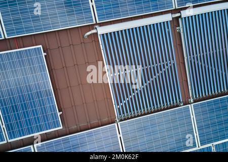 Gebäudedach mit Reihen von blauen Photovoltaik-Paneelen und Vakuum-Luft-Solarkollektoren für die Warmwasserbereitung und die Produktion von sauberem ökologischem Strom Stockfoto