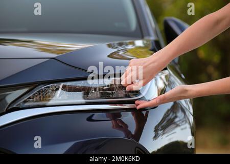 Weibliche Hände der Fahrerin überprüfen den Scheinwerfer ihres neuen Autos. Kauf des Fahrzeugkonzepts Stockfoto
