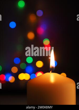 Eine weiße Kerze brennt mit bunten Weihnachtslichtern im Hintergrund, Platz für Text Stockfoto