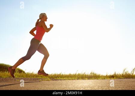 Vor Sonnenuntergang joggen. Eine junge Frau läuft an einem sonnigen Tag. Stockfoto