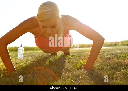Damit jeder Muskel strafft wird. Eine junge Frau, die Liegestütze auf einem Feld macht. Stockfoto