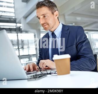 Wir planen etwas. Ein in Anzügen verkleideter, erwachsener Geschäftsmann, der seinen Laptop benutzt, während er an einem Tisch sitzt und Kaffee trinkt. Stockfoto