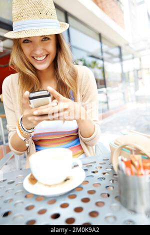 Dieses Restaurant bekommt eine gute Bewertung. Eine zwanglose junge Frau, die eine SMS schickt, während sie in einem Straßencafé in der Stadt sitzt - Porträt. Stockfoto