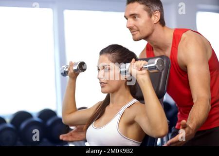 Ich helfe dir. Ein Trainer, der einer jungen Frau beim Gewichtheben hilft. Stockfoto