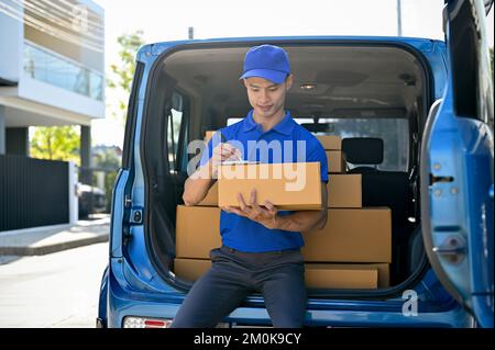 Junger asiatischer Liefermann, der Bestellungen mit einem Tablet prüft, bevor er das Paket an den Kunden übergibt. Konzept des Lieferservice Stockfoto