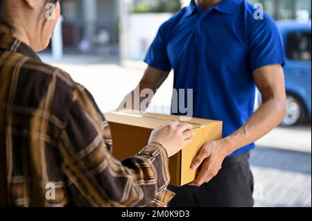 Verkürzt zu wenig Liefermann in blauer Uniform, der das Paket an den Kunden übergibt. Konzept des Lieferservice Stockfoto