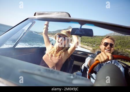 Fahren wir einfach weiter. Ein glückliches junges Paar, das an einem schönen Sommertag in einem Cabrio fährt. Stockfoto