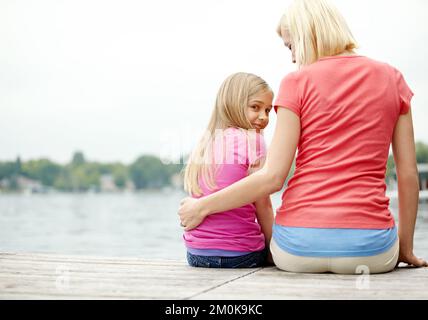 Ein bisschen Zeit miteinander verbringen. Ein Bild von einer Mutter und Tochter, die am Fluss sitzen. Stockfoto