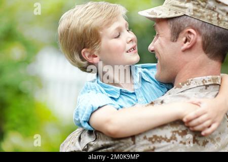 Es ist so schön, zu Hause zu sein. Ein Vater, der von der Armee zurückgekehrt ist und seinen Sohn hält, während sein Vater ihn mit Kopierraum ansieht. Stockfoto