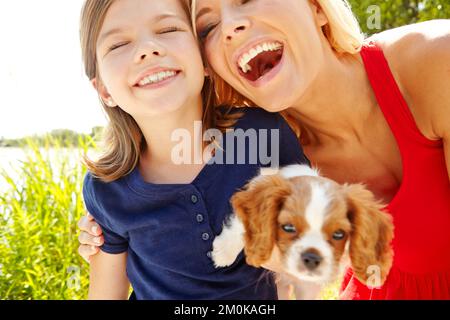 Schöne Zeit mit mom und dem Welpen. Eine glückliche Mutter und Tochter, die einen süßen Welpen halten, während sie draußen stehen. Stockfoto