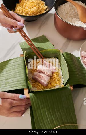 Nahaufnahme einer Frau, die Schweinefleischstücke in quadratischen Kuchen für die Tet-Feier einfügt Stockfoto