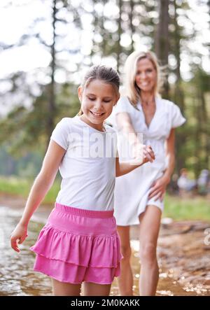 Wir gehen hier lang, mom. Ein süßes kleines Mädchen, das mit ihrer Mutter durch einen Wildnisstrom läuft. Stockfoto