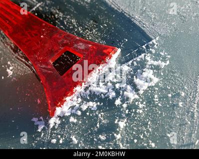 Roter Schaber entfernt Eis von der Windschutzscheibe des Autos, Nahaufnahme Stockfoto