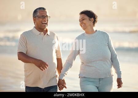Ein älteres gemischtes Paar, das am Strand zusammen am Strand spazierenging und lächelte und lachte an einem Tag am Strand. Hispanische Ehemann und Ehefrau schauen glücklich und Stockfoto