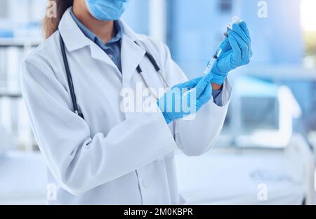 Eine Ärztin, die eine Dosis des Medikaments in einer Spritze zubereitet, während sie eine Maske und einen Labormantel in einem Krankenhauszimmer trägt. Bereit zur Verabreichung eines Stockfoto