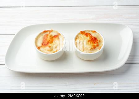 Gebackene Julienne mit Pilzen und Käse auf weißem Teller Stockfoto