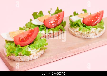 Reiskuchen-Sandwiches mit Tomaten, Salat und Ei auf Holzbrett. Einfaches Frühstück. Diät-Essen. Schnelle und gesunde Sandwiches. Knäckebrot mit leckerer Füllung. Gesunder Ernährungs-Snack Stockfoto