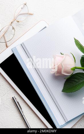 Flach liegender Büroschreibtisch für Frauen. Weiblicher Arbeitsplatz mit pinkfarbenem Blumenstrauß, Milchprodukte, Gläser Stockfoto