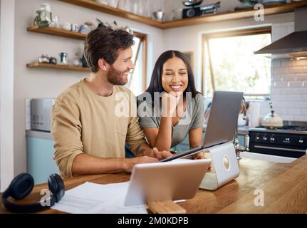 Glücklicher junger Kaukasier, der an einem Laptop arbeitet, während seine Frau neben ihm steht und auf den Bildschirm schaut. Ein Mann, der freiberuflich arbeitet und abgelenkt wird Stockfoto