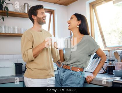 Ein liebenswertes junges gemischtes Paar, das seinen Morgenkaffee trinkt und sich zu Hause in der Küche unterhält. Junge Männer und Frauen, die glücklich darüber sind Stockfoto