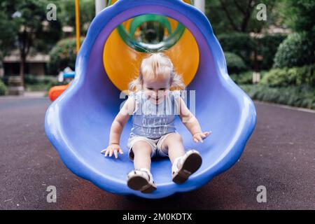 Süßes, blondes, weißes Mädchen, das im Sommer auf dem Spielplatz spaziert. Stockfoto