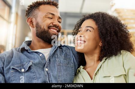 Ein junges gemischtes Paar lächelt, während es sich auf der Couch zuhause in die Augen starrt. Glücklicher lateinamerikanischer Freund und Freundin, die auf dem Sofa sitzen Stockfoto