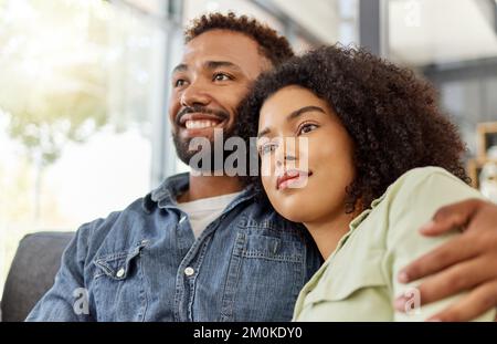 Ein junges gemischtes Paar, das sich umarmt, während es zu Hause auf der Couch fernsieht. Lateinamerikanischer Freund und Freundin sitzen und entspannen sich auf dem Sofa Stockfoto