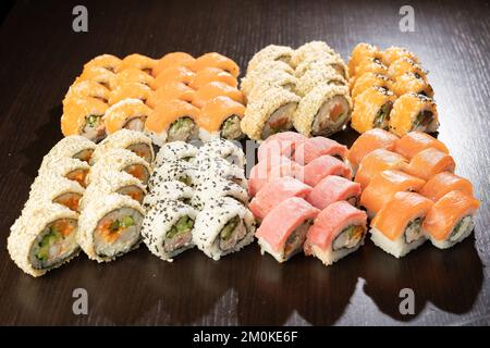 Sushi-Brötchen mit Lachs, Aal, Thunfisch, Avocado, königlicher Garnele, Frischkäse-Philadelphia auf schwarzem Steinbrett. Speicherplatz kopieren Stockfoto