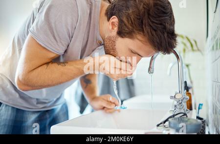 Ein hübscher Mann, der sich zu Hause in einem Badezimmer den Mund spült. Kaukasischer Mann mit Mundwasser für frischen Atem in seiner Wohnung Stockfoto