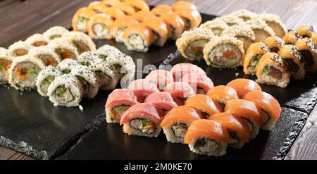 Rainbow Sushi Roll Set mit Lachs, Aal, Thunfisch, Avocado, königlicher Garnele, Frischkäse-philadelphia auf schwarzem Steinbrett. Speicherplatz kopieren Stockfoto