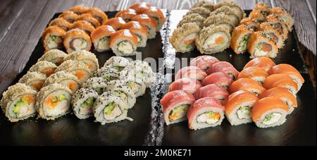 Rainbow Sushi Roll Set mit Lachs, Aal, Thunfisch, Avocado, königlicher Garnele, Frischkäse-Philadelphia auf schwarzem Steinbrett. Speicherplatz kopieren Stockfoto