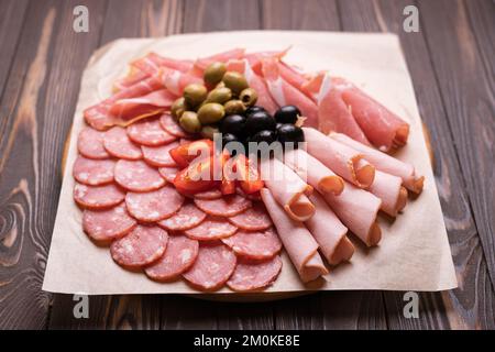 Kaltgeräucherte Fleischplatte mit Wurst, Schinkenscheiben, Prosciutto, Speck, Oliven, Tomaten. Vorspeise auf weißem Teller. Speicherplatz kopieren. Stockfoto