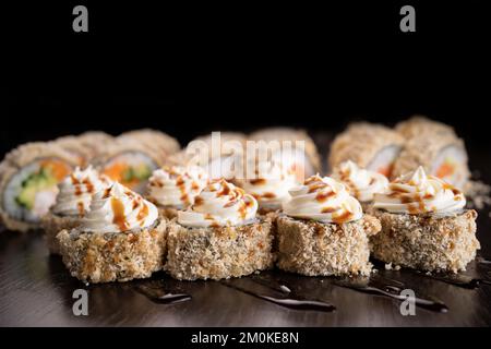 Warme Sushi-Brötchen, frittierter dekorierter Frischkäse. Auswahl an köstlichem Tempura und gebackenem Sushi mit Lachs. Sushi-Vulkan auf schwarzem Hintergrund. Stockfoto