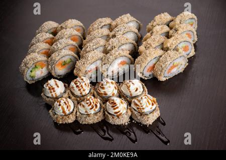Tempura Maki Roll auf schwarzem Hintergrund. Warmes Sushi mit Lachs, Krabben und Gurken, mit Sauce garniert. Modernes japanisches Speisenkonzept. Stockfoto