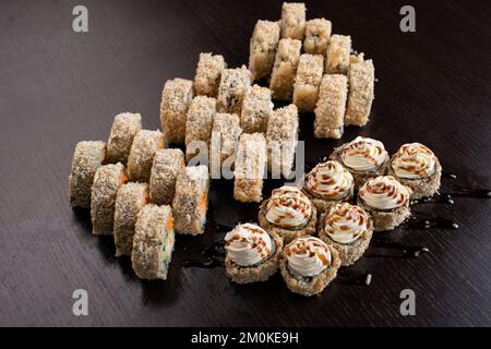 Japanische Tempura-Sushi-Brötchen auf schwarzem Hintergrund mit Reflexion. Sushi-Stücke mit Lachs, Aal, Gurke, Frischkäse, Avocado in Reis verpackt Stockfoto