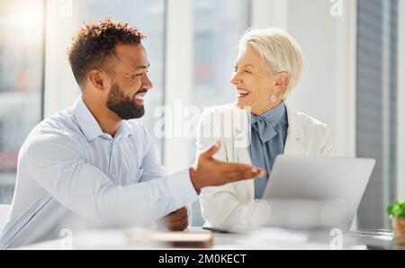 Zwei lächelnde Kollegen, die an einem Notebook in einem Büro zusammenarbeiten. Fröhlicher junger gemischter Geschäftsmann, der sich mit einem reifen Weißen trifft Stockfoto