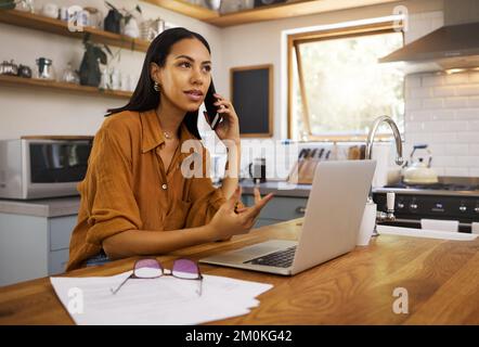 Junge, ernsthafte Geschäftsfrau gemischter Rassen, die während eines Telefonats Papier und Rechnungen durchsucht und zu Hause an einem Laptop arbeitet. Ein hispanic Stockfoto