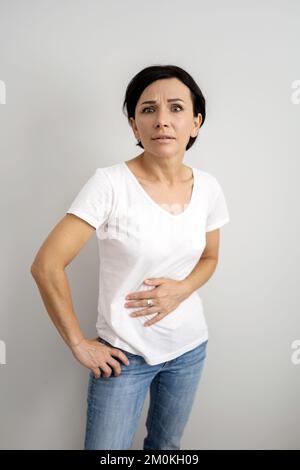 Frauen mittleren Alters leiden an Bauchschmerzen. Eine Frau, die ihren Magen vor Schmerzen hält Stockfoto