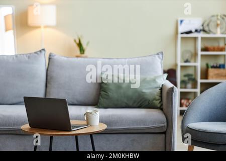 Nahaufnahme eines Laptops auf dem Couchtisch im stilvollen Wohnzimmer mit komfortablen Möbeln und Kopierraum Stockfoto