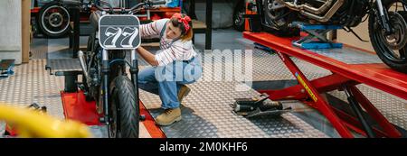 Eine Mechanikerin, die ein Motorrad in der Fabrik überprüft Stockfoto