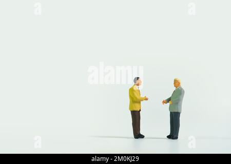Die zwei Miniaturfiguren von Geschäftsleuten, die eine Diskussion auf weißem Hintergrund führen Stockfoto
