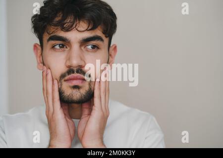 Mann berührt Bart und Gesicht, gesunde Haut. Hautpflege im Badezimmer. Männerporträt. Gesundheitsfürsorge. Stockfoto