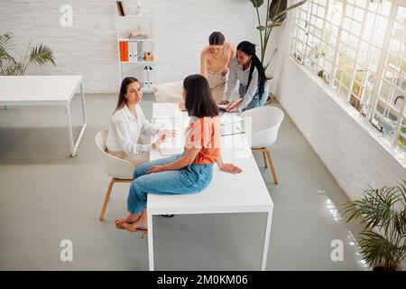 Eine vielfältige Gruppe von Geschäftsfrauen von oben bespricht Pläne, während sie gemeinsam an einem Tisch in einem Büro arbeiten. Gemeinkosten von Kollegen am Arbeitsplatz Stockfoto