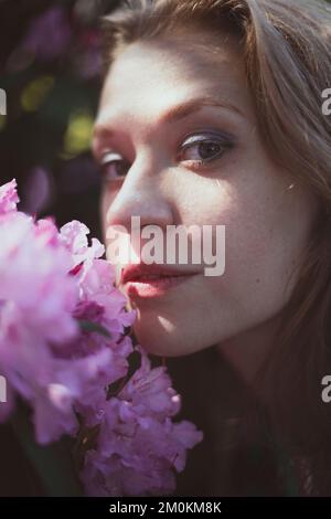Nahaufnahme Frau, die die Wange gegen den Strauch drückt, mit pinkfarbenen Blumen im Porträt Stockfoto