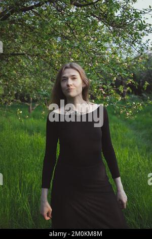 Eine Frau trägt ein eng anliegendes schwarzes Kleid in einer Gartenfotografie Stockfoto