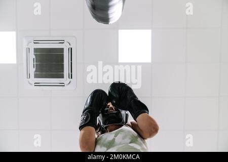 Junge Frau trägt schwarze Boxhandschuhe in Wächterposition vor einem Boxsack im Fitnessstudio Stockfoto