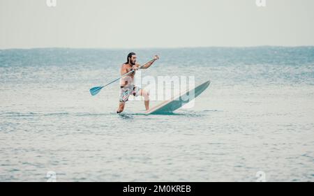 Seemannssup. Asiatischer Sportler schwimmt im Meer und paddelt im Sommer bei Sonnenuntergang. Gesunder starker Mann genießt aktiven Outdoor-Lebensstil und Wasser Stockfoto