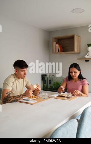 Zwei junge lateinische Menschen essen traditionelle Arepas im Wohnzimmer. Stockfoto