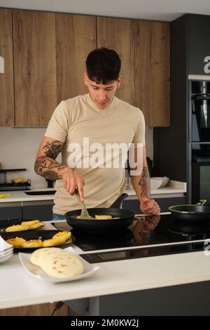 Junger ecuadorianischer Mann, der Lappingachos in einer Pfanne kocht. Stockfoto